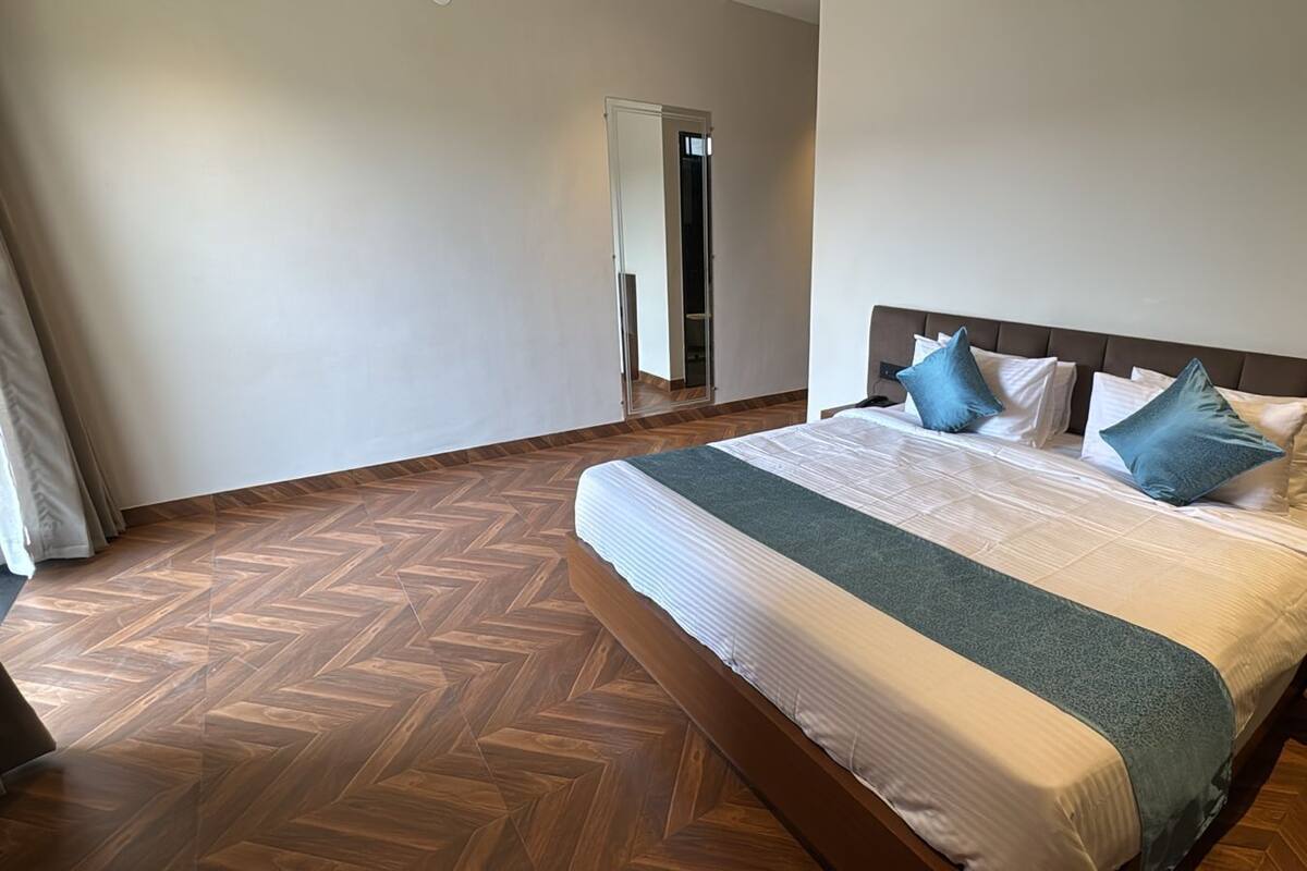 A bedroom with a large bed, a wooden herringbone floor, a nightstand, and a wardrobe.