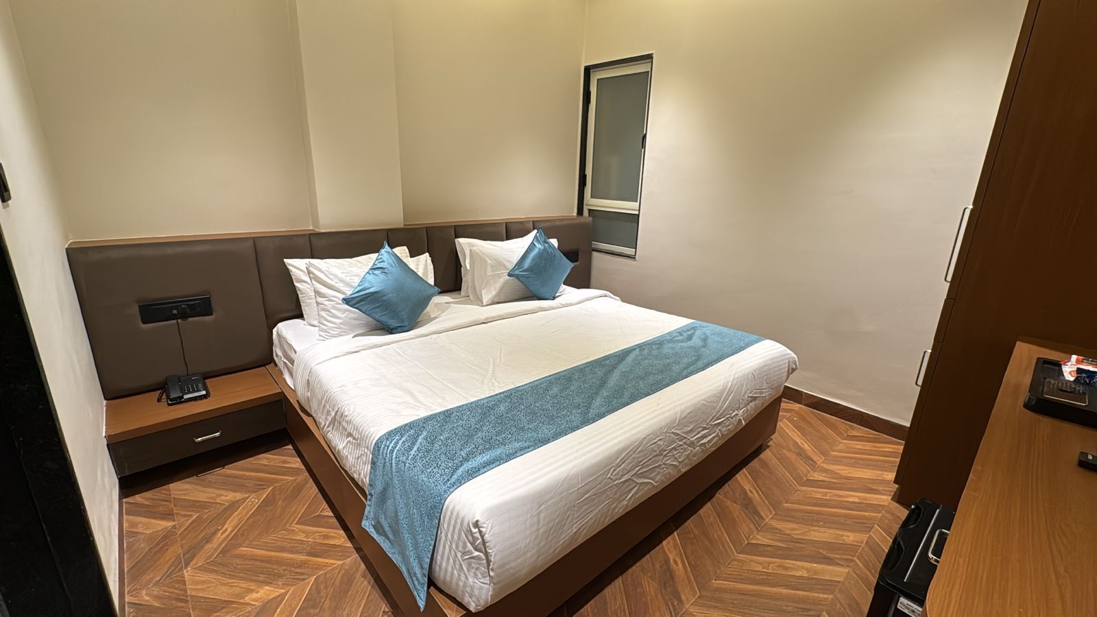 Una habitación de hotel con una cama, una mesita de noche, un enchufe y una puerta.