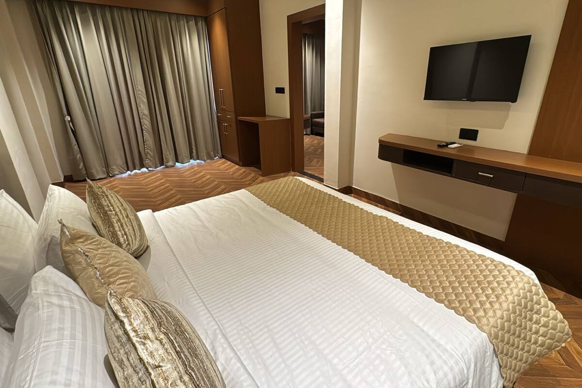 A hotel room with a large bed, a TV mounted on the wall, and a wooden desk.
