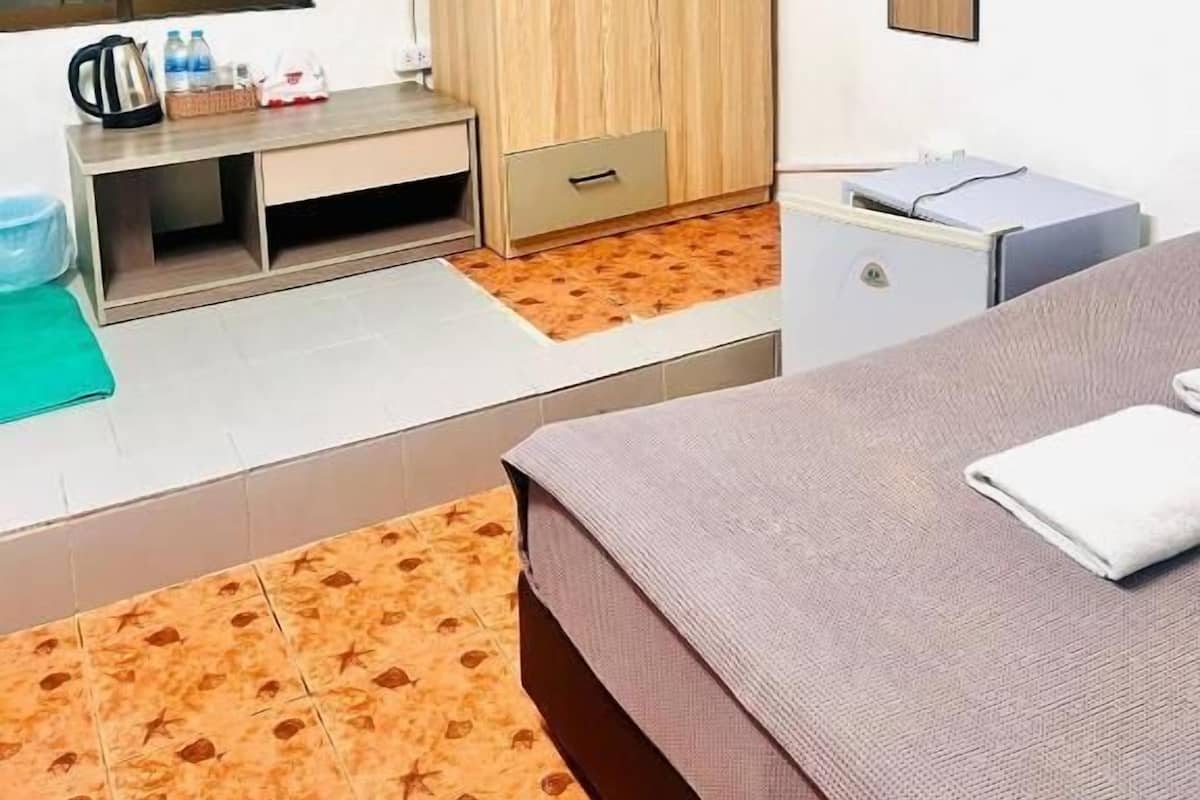 A hotel room with a bed, a desk, a wardrobe, a mirror, and an air conditioning unit.