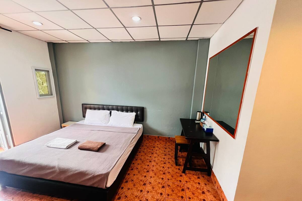 A bedroom with a bed, a desk, and a mirror.