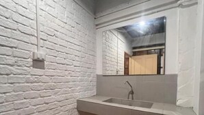 A bathroom with a white brick wall, a wooden floor, a sink, and a mirror. - Patong Adventure Hostel (Patong)