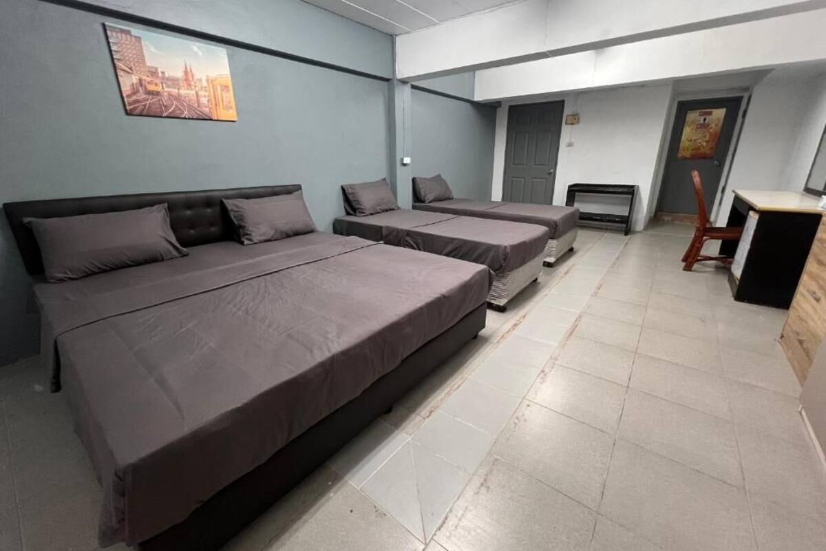 A room with three beds, a desk, a chair, a door, and a painting on the wall.