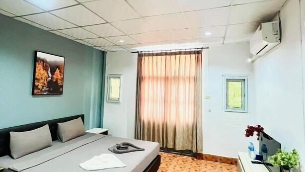 A hotel room with a bed, a desk, an air conditioner, a window with curtains, and a painting on the wall. - Patong Adventure Hostel (Patong)