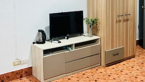A room with a television on a wooden stand, a cabinet with drawers, a small plant, and a tiled floor. - Patong Adventure Hostel (Patong)