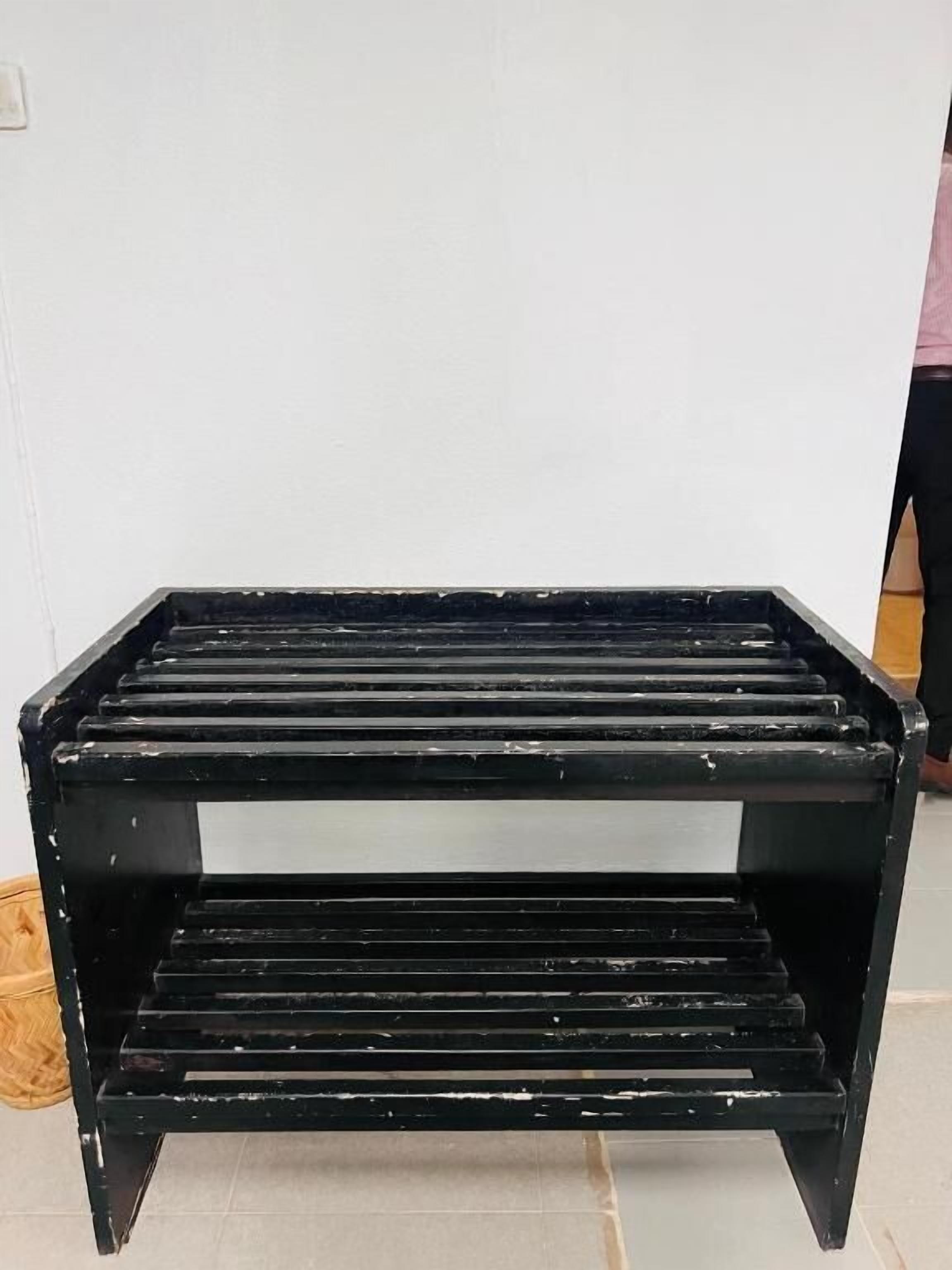 Un banco negro con varias listones horizontales frente a una pared lisa.
