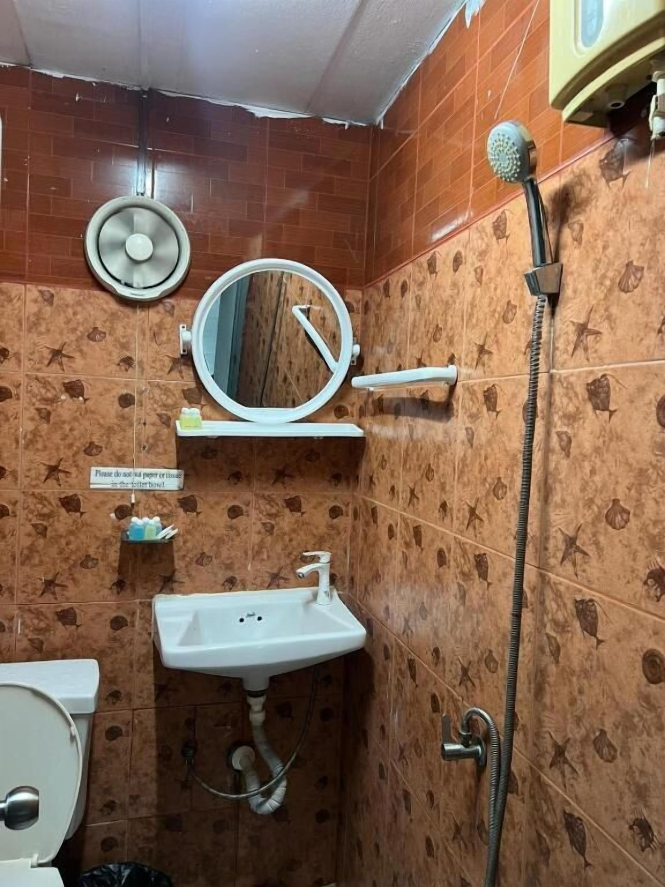 A bathroom with a toilet, sink, mirror, shower, and a fan.