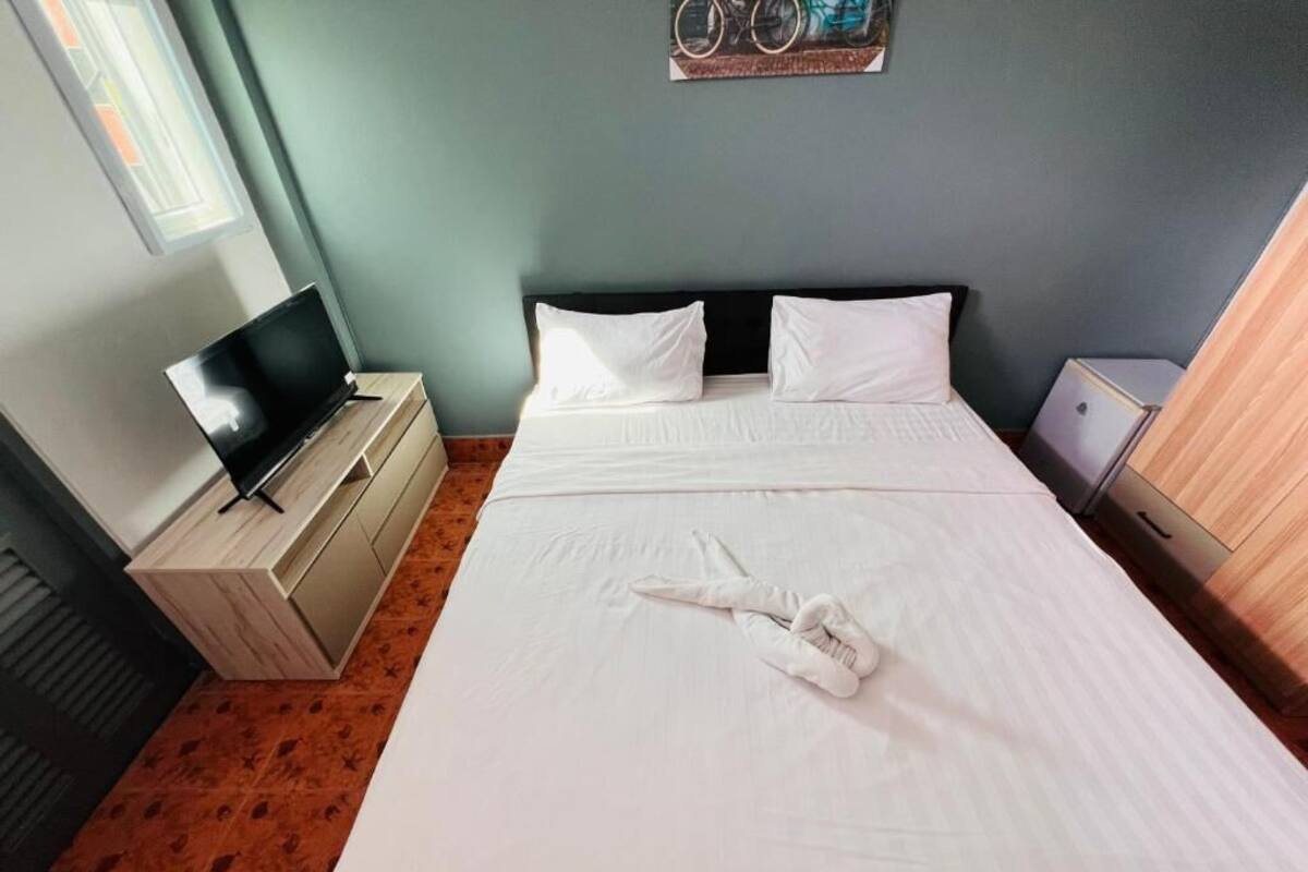 A hotel room with a bed, a TV on a wooden dresser, a wall-mounted artwork, and a window.