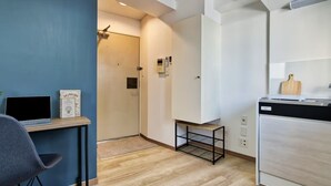 A compact kitchen with a modern design, featuring a built-in dishwasher, a small table with a laptop, and a chair. - Modern Living Tokyo Komagome 508, a compact studio at excellent location (豊島区 駒込)