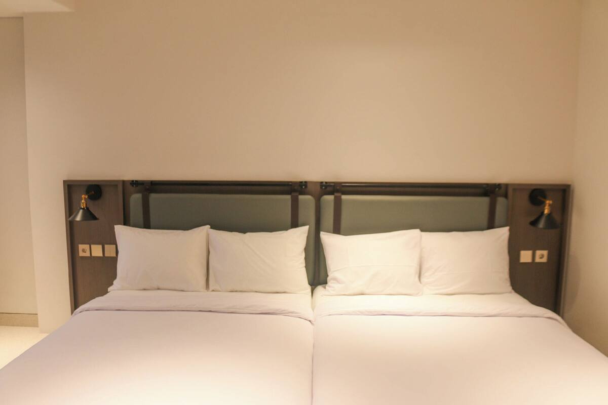 A double bed with white linens, a wooden headboard, and two bedside lamps.