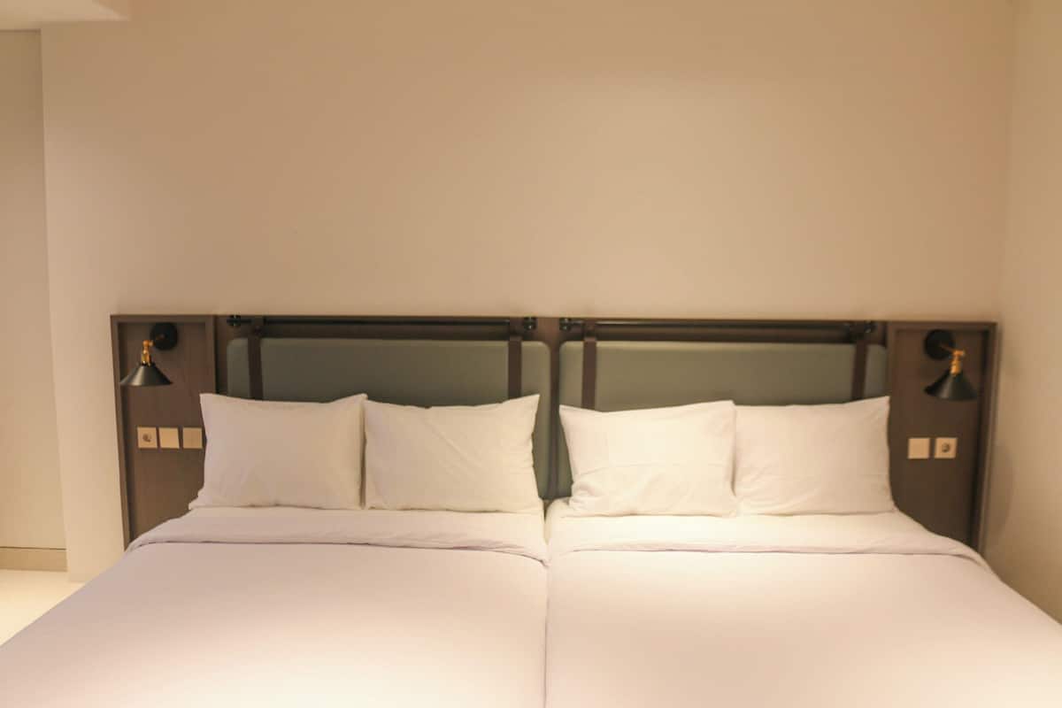 A double bed with white linens, a wooden headboard, and two bedside lamps.