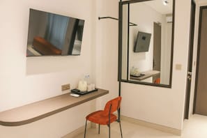 Une chambre d’hôtel équipée d’un téléviseur à écran plat fixé au mur, d’une petite table avec une chaise et d’un miroir qui reflète une partie de la pièce.