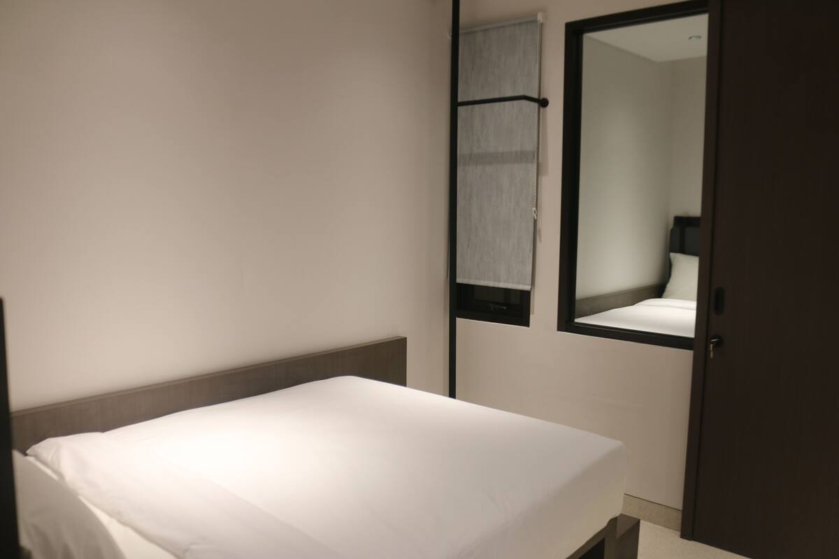 A hotel room with a single bed, a mirror, and a door.