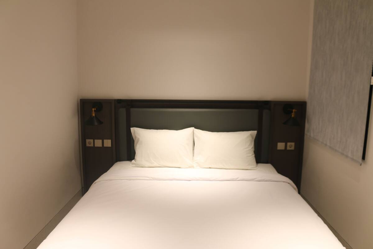 A neatly made bed with white linens and a dark headboard.
