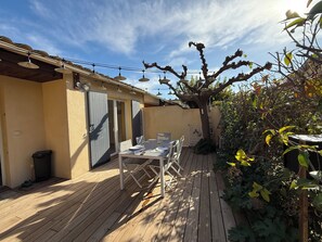 Eine Holzterrasse mit Tisch und Stühlen, ein überdachter Bereich mit Decke und ein Baum mit wenigen Blättern.