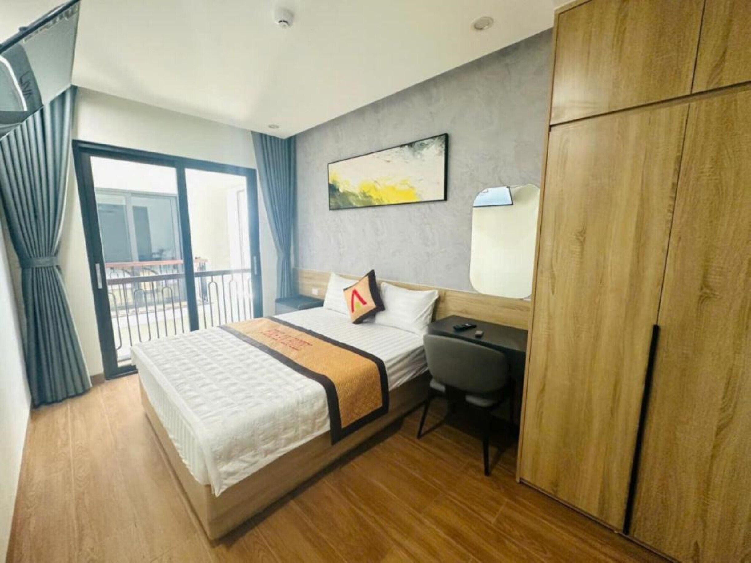 A hotel room with a bed, a desk, a wardrobe, a window with curtains, and a painting on the wall.