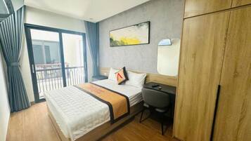 A hotel room with a bed, a desk, a wardrobe, a window with curtains, and a painting on the wall.