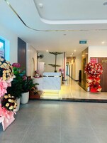 Zona de recepción de hotel con mostrador de mármol, plantas en macetas y decoración floral.