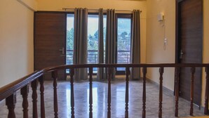 A hotel room with a wooden staircase, a large sliding glass door, and a view of greenery outside. - Pinewood Manor Kasauli (Solan)