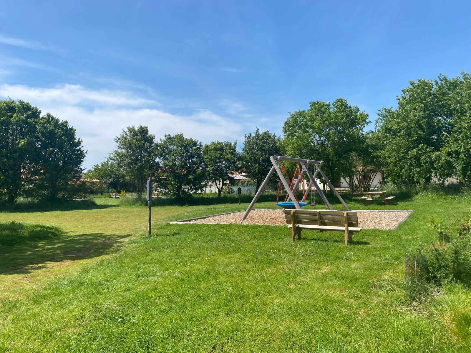 A park with a swing set, picnic table, and benches.