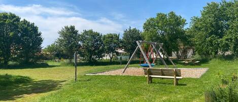 A park with a swing set, picnic table, and benches.