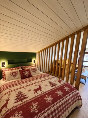 A bedroom with a checkered bedspread featuring deer and snowflakes, a wooden headboard, and a green wall. - Le Bois Gentil 3* - lounge + sleeping area, pets welcome (La Clusaz)