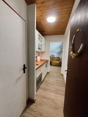A narrow hallway leading to a kitchen with white cabinets and a wooden ceiling. - Le Bois Gentil 3* - lounge + sleeping area, pets welcome (La Clusaz)