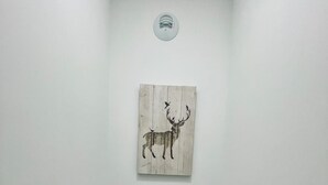 Un bany petit amb vàter blanc, terra de fusta, llum penjant a la paret i una obra d'art de fusta amb un cervol.