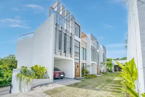A modern residential building with a car parked in the driveway, surrounded by greenery. - Snow White Villa 2 3-Bedroom Haven near the Beach (Badung Regency Bali)