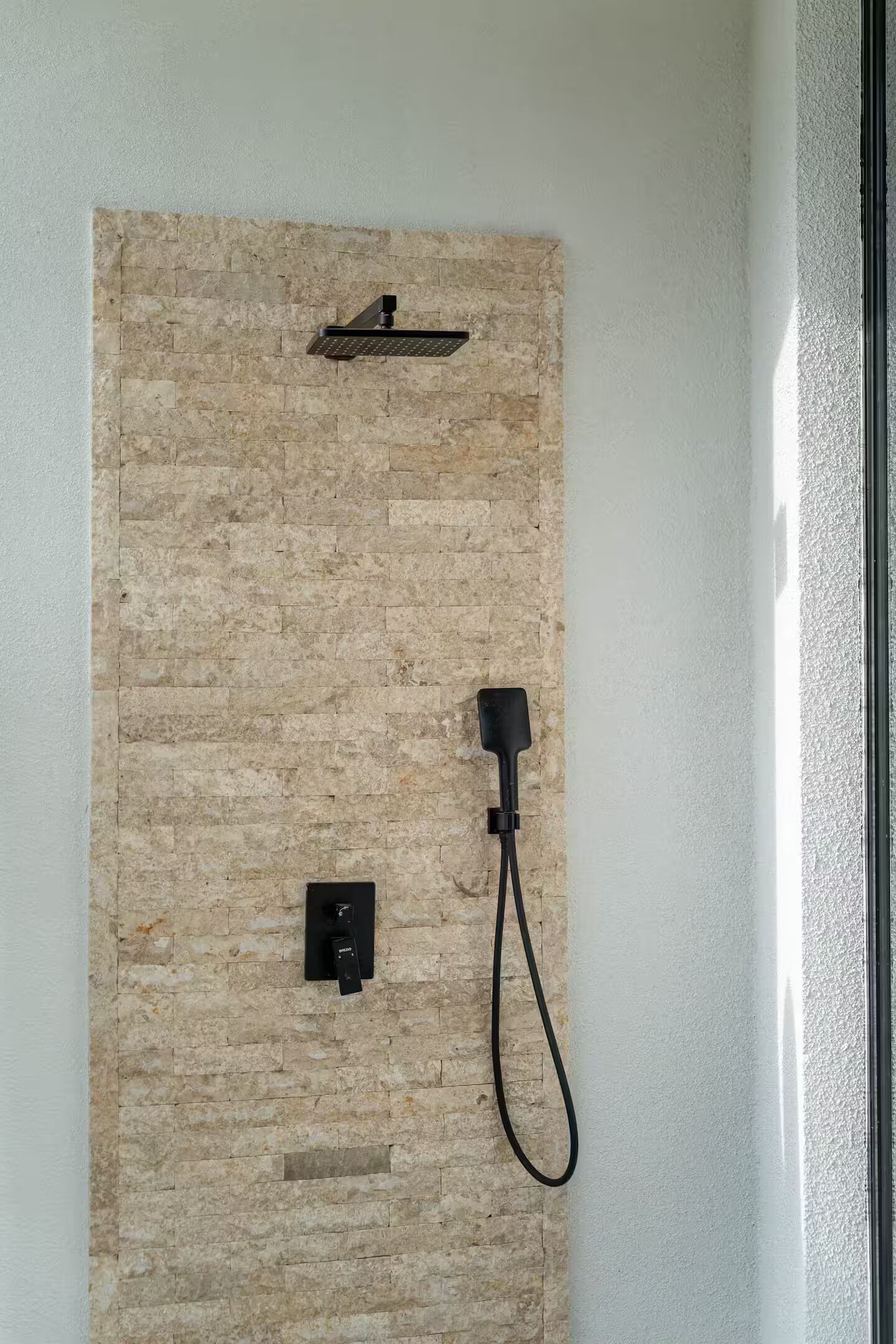 A shower area with a stone wall, a handheld showerhead, and a power outlet.