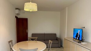 Un salon comprenant une table ronde, quatre chaises, un canapé, un téléviseur et un meuble.