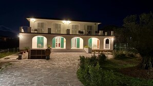 Un bâtiment à deux étages, doté d’une entrée pavée de pierres, de fenêtres en arc de cercle et d’un espace extérieur aménagé pour s’asseoir.