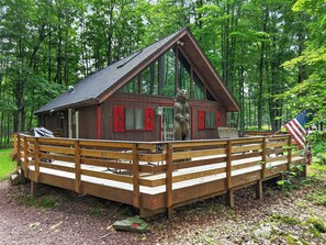 Eine Holzhütte mit einer Terrasse, einer Bärenstatue und einer amerikanischen Flagge.