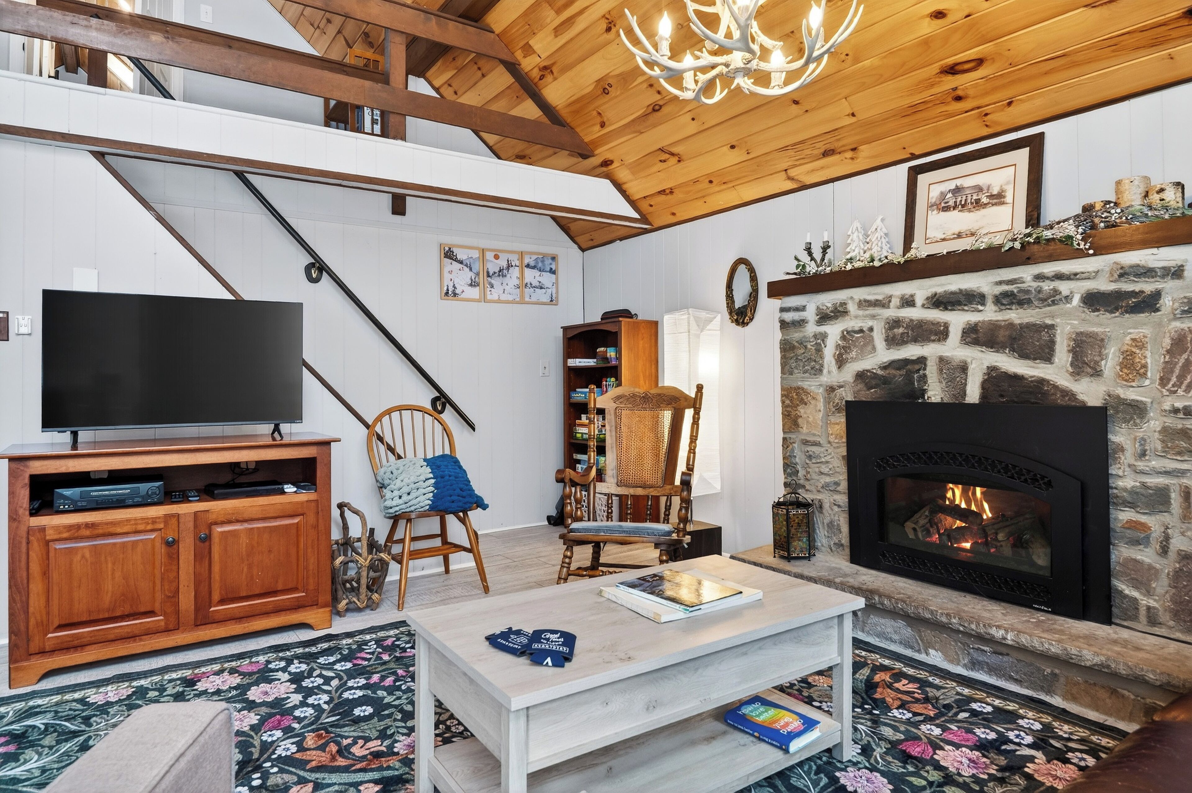 Un salon chaleureux avec une cheminée en pierre, des meubles en bois, un téléviseur à écran plat et un escalier.