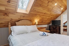 A bedroom with a wooden ceiling, a bed with white bedding, a nightstand, a TV, and a small table. - Wooded Poconos Cabin • Fireplace + Deck + Firepit • Near Jack Frost + Kalahari (Pocono Lake)