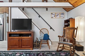 A living room with a wooden entertainment unit, a television, a rocking chair, and a staircase. - Wooded Poconos Cabin • Fireplace + Deck + Firepit • Near Jack Frost + Kalahari (Pocono Lake)
