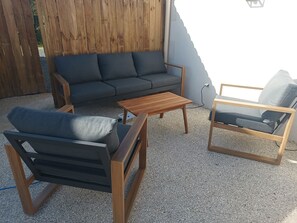 A patio area with a wooden fence, a grey sofa, a wooden coffee table, and a wooden chair with cushions. - Gîte 4 people, air-conditioned, swimming pool, 30mn Puy du Fou, with family or friends. (Chantonnay)