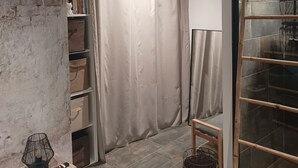 A room with a brick wall, a curtain, a shelf with books, a small table with a lamp, and a woven basket. - Gîte 4 people, air-conditioned, swimming pool, 30mn Puy du Fou, with family or friends. (Chantonnay)