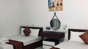 Habitación de hotel con dos camas individuales, una mesita de noche pequeña con un espejo, una botella de agua y un cuadro en la pared.