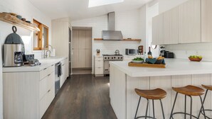 Une cuisine moderne avec des meubles blancs, un îlot central doté de tabourets, un four encastré et un four à micro-ondes.