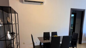 En matplats med ett bord och stolar, en svart hylla med diverse föremål och en luftkonditioneringsenhet på väggen.