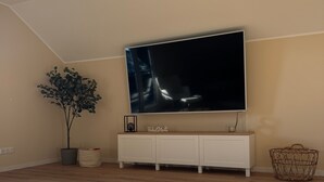 Una habitación con un televisor de pantalla plana grande montado en la pared, una consola blanca debajo, una planta en maceta y una cesta de mimbre.