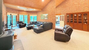 A spacious living room with a brick wall, a sectional sofa, leather chairs, and a wooden ceiling. - Spacious Queen + Single Farmhouse Room (Worrigee)