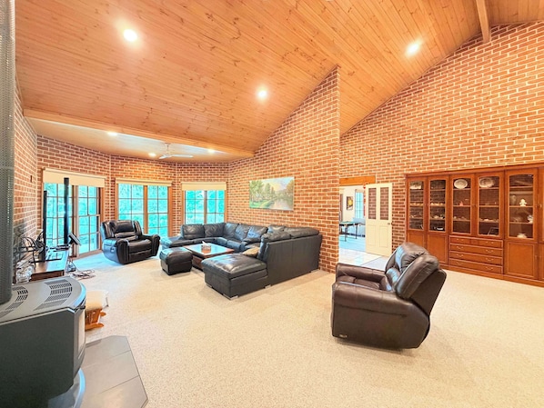 Ein geräumiges Wohnzimmer mit Backsteinwand, Ecksofa, Ledersesseln und Holzboden.