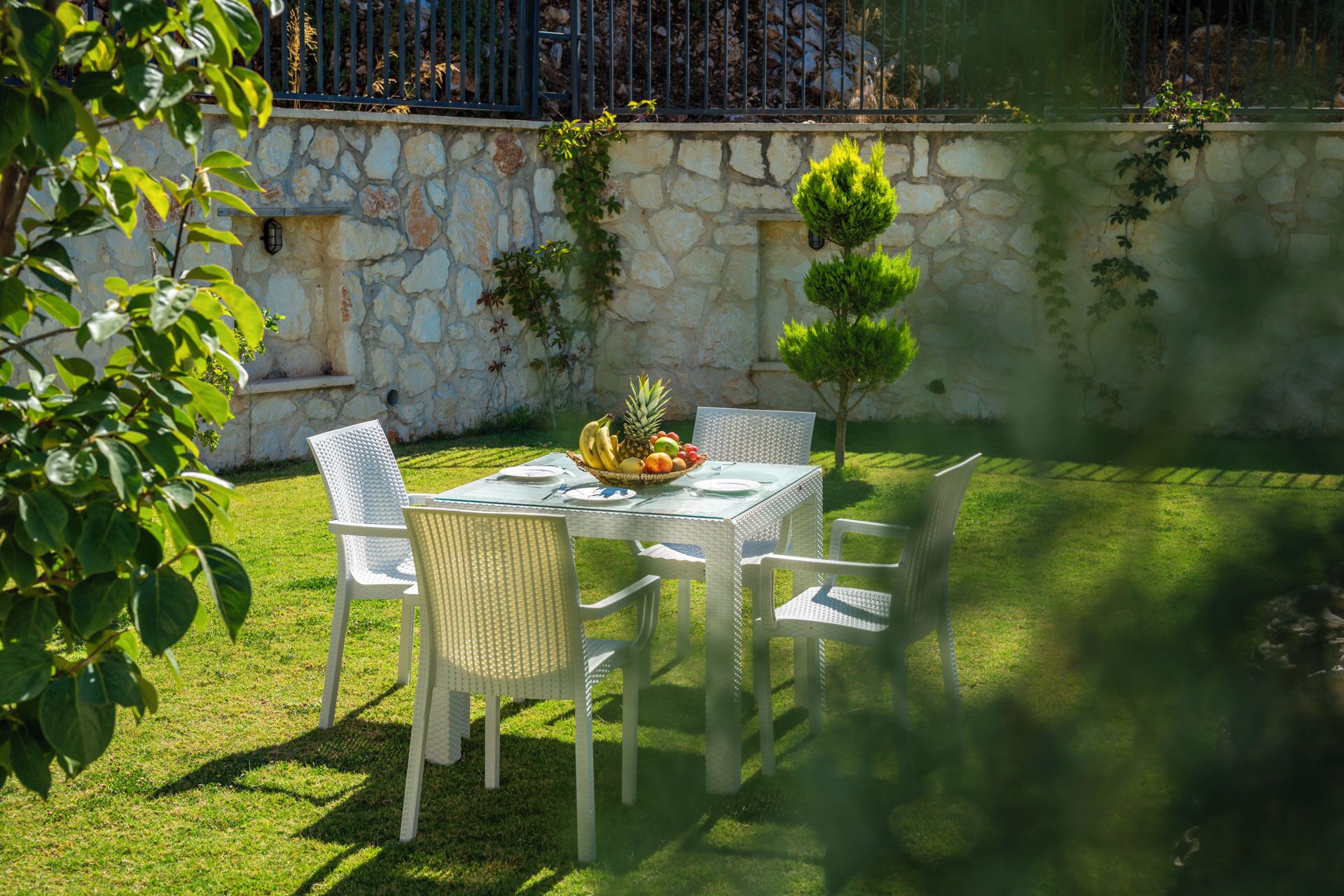 A stone wall, a small tree, and a table with chairs in a garden.