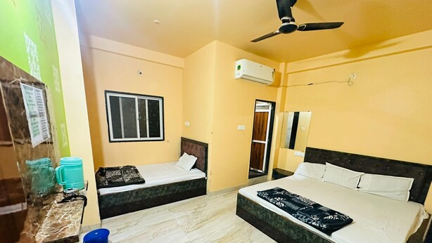Quarto de hotel com duas camas, ventilador de teto, ar condicionado, janela e uma pequena mesa com uma xícara azul.