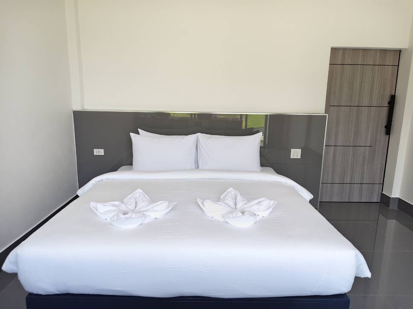 Una cama bien hecha con sábanas blancas y dos toallas dispuestas en un diseño floral sobre la colcha.