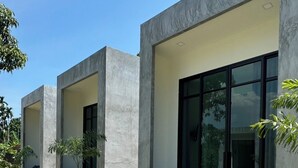 A modern building with large glass windows and concrete pillars. There are outdoor seating areas with lounge chairs. - Pearlix Koh Mook (Ko Mook)