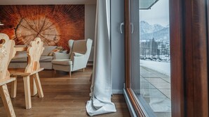 Ein modernes Wohnzimmer mit Holzboden, einem großen Fenster mit Blick auf schneebedeckte Berge und einer Wand mit großformatiger Holzstruktur-Kunst.