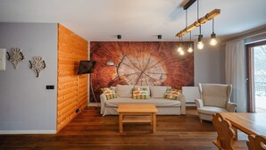 Ein modernes Wohnzimmer mit Holzboden, einer Couch mit bunten Kissen, einem Holztisch und einer großen Wandmalerei.